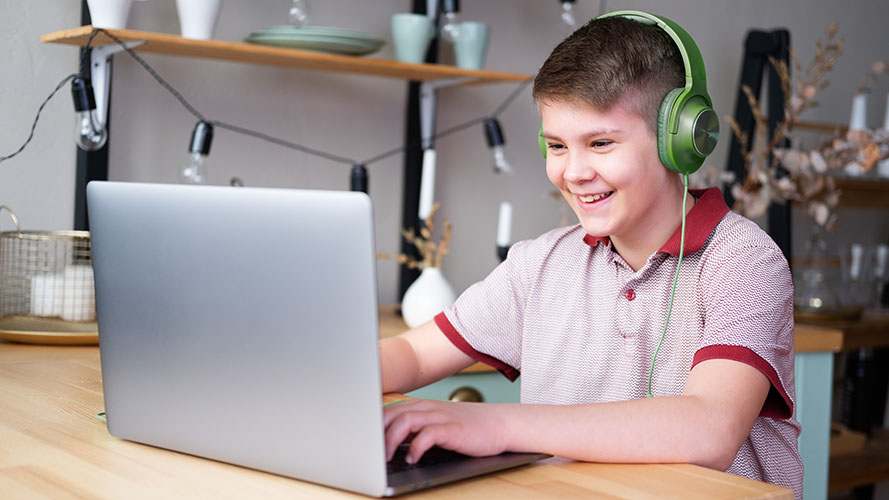 Young student working on laptop wearing green headphones