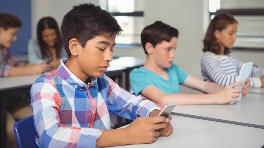 High school students in classroom reading on smartphones.