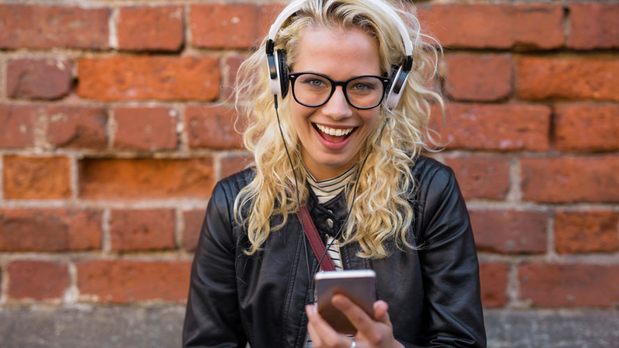 Smiling student, wearing headphones and holding a smartphone