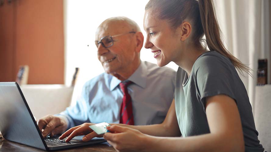 Young lady and older man looking at a laptop together, smiling