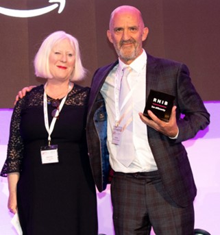 Noel Duffy with Anna Tyler on stage after the award was presented. Noel holds his award and has an arm round Anna